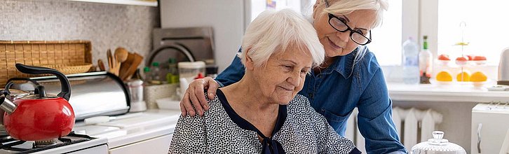 Eine Frau hilft einer demenzerkrankten Seniorin im Haushalt.